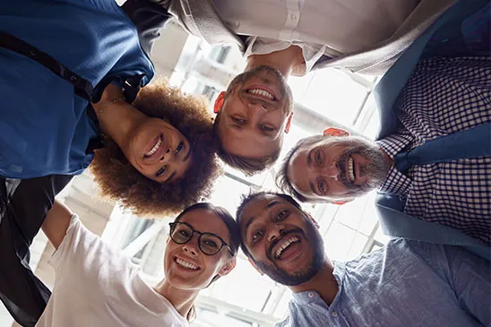 Um grupo de trabalhadores se abraçando vistos de baixo proa cima dentro da roda formada pelo abraço.