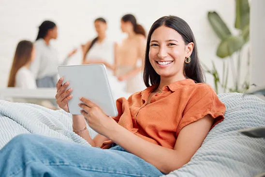 Uma Profissional feliz em trabalhar na Tange, morena vestindo uma camiseta laranja e uma calça jeans, segurando um tablet.